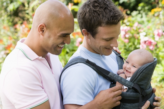 Gay couple holding baby in shoulder bag and smiling